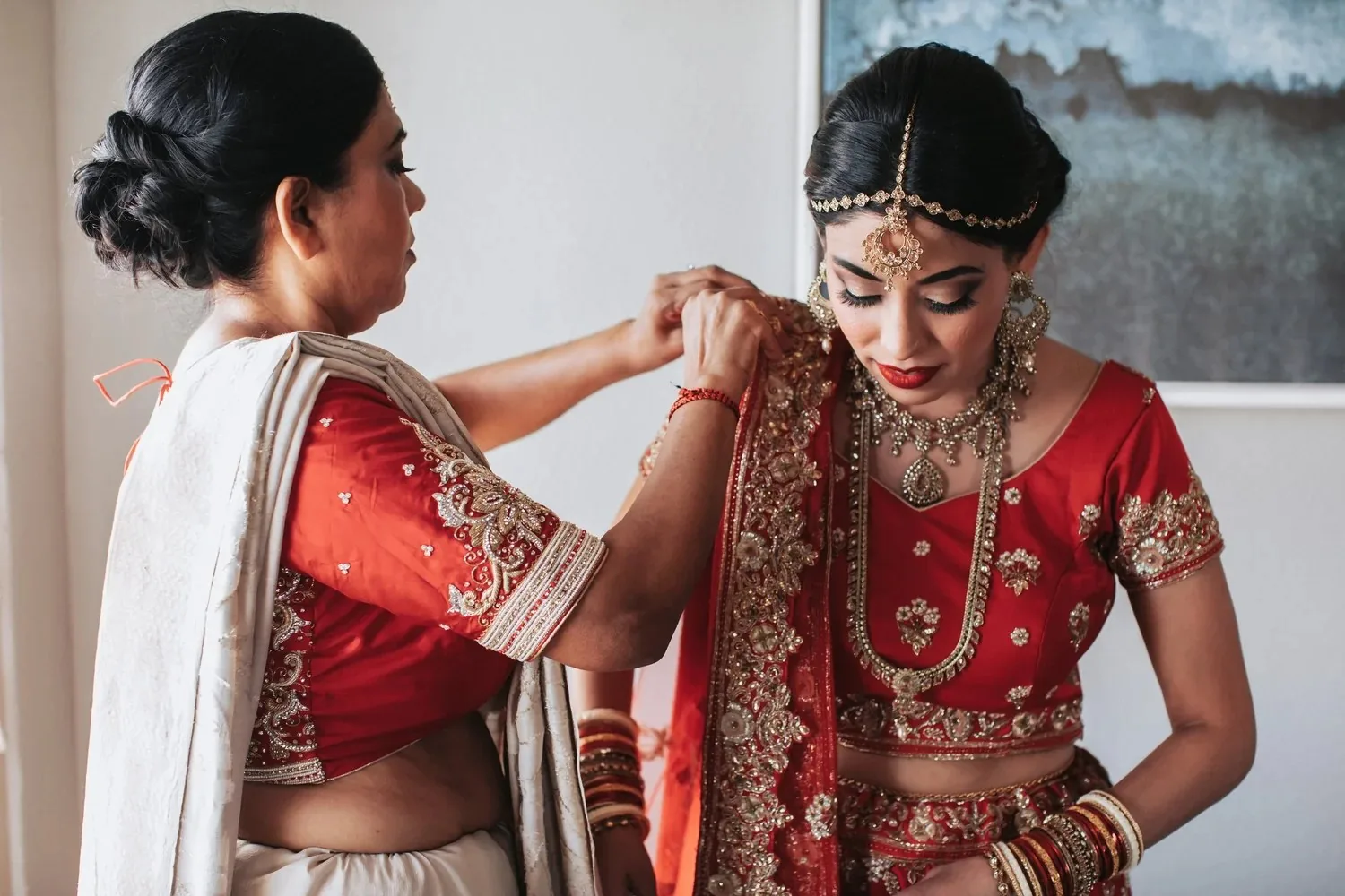 Bride in red wedding attire being helped with jewelry